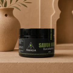 Jar of 'Savon Noir' with 'Amalia' branding on a beige surface with decorative elements.