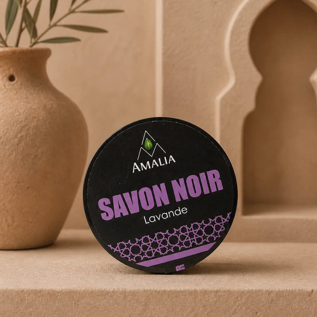 Amalia Savon Noir Lavande soap bar on a beige surface with a decorative vase and plant in the background.