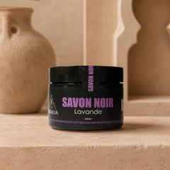 Jar of Savon Noir Lavande on a beige surface with decorative elements